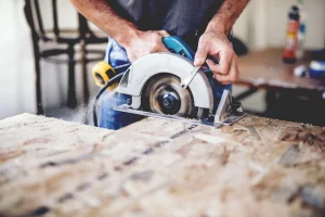 Carpenter using circular saw for cutting wooden boards. Construction details of male worker or handy man with power tools